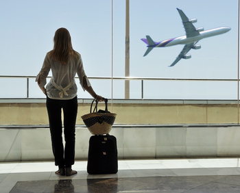 woman with carry on luggage at airport, plane in background